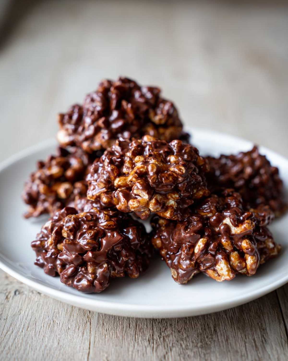 A stack of shiny, rich No-Bake Chocolate Covered Pretzel Clusters piled on a white plate.