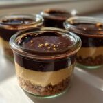 Four individual No-Bake Chocolate Peanut Butter Pie Jars featuring crust, peanut butter filling, and chocolate topping, sitting in sunlight.