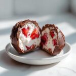 A No-Bake Chocolate Strawberry Yogurt Cluster cut in half showing creamy yogurt filling and fresh strawberries inside a chocolate shell.