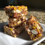 A stack of four dense No-Bake Lemon Almond Date Bars studded with sliced almonds and yellow zest.
