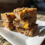 A stack of four No-Bake Lemon Almond Date Bars featuring visible oats, almonds, and bright yellow lemon zest.