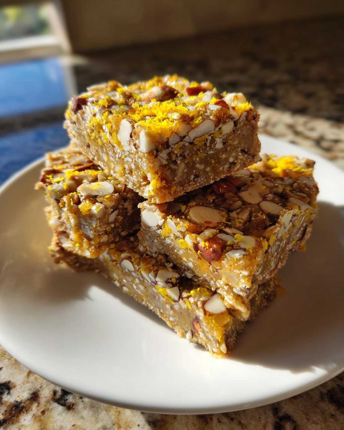 A stack of four No-Bake Lemon Almond Date Bars topped with chopped almonds and bright yellow zest.