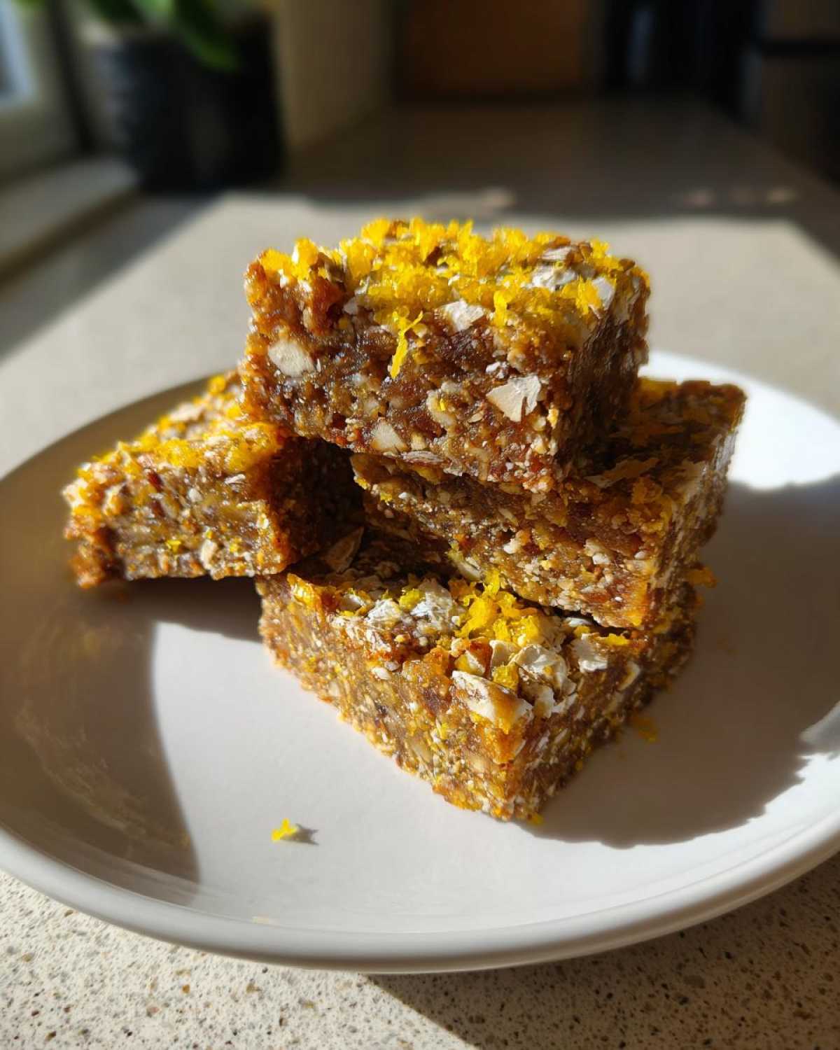 Close-up of three stacked No-Bake Lemon Almond Date Bars topped with bright yellow lemon zest.