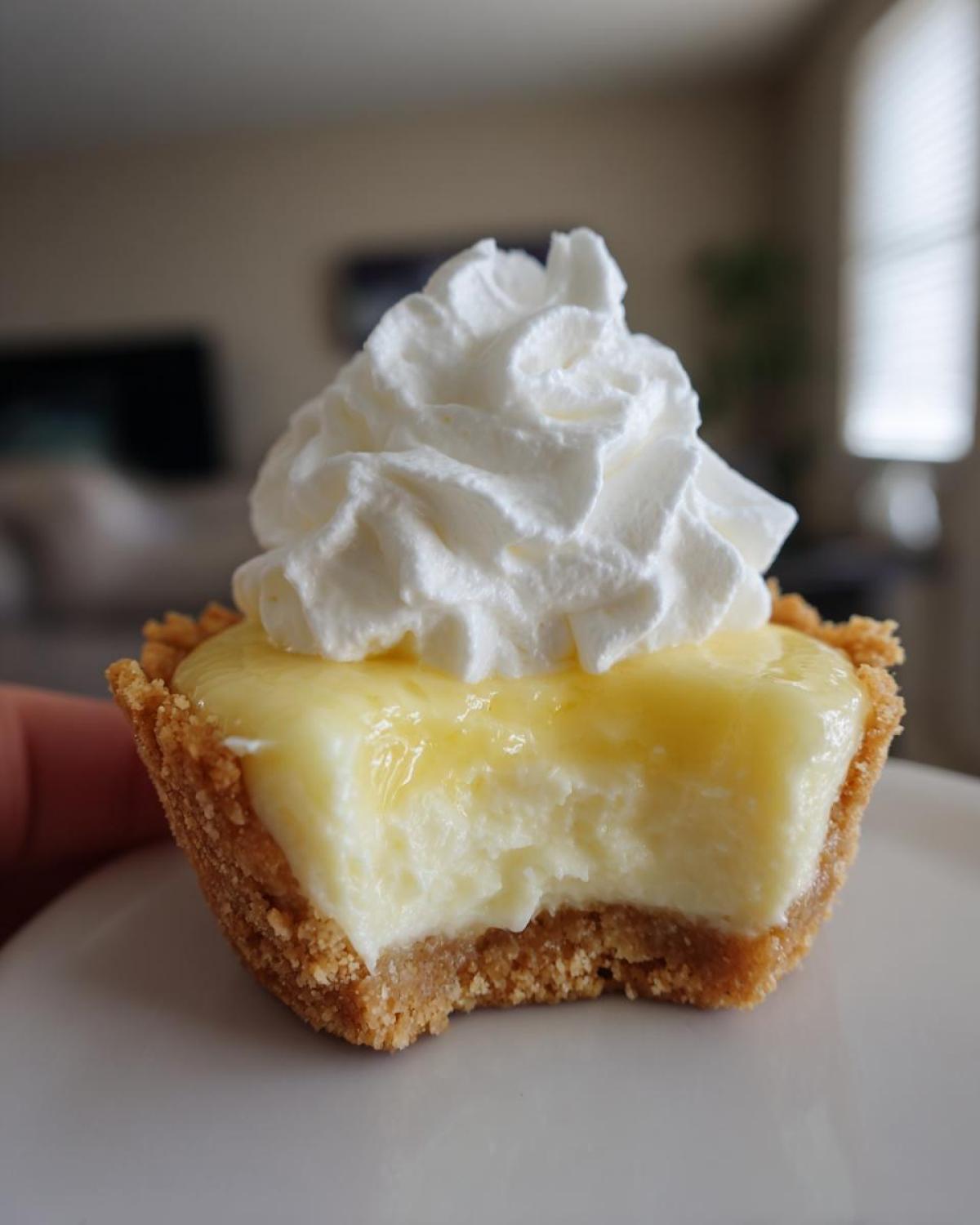 A close-up of a No-Bake Lemon Cream Pie Cup with a bite taken out, showing the creamy filling and graham cracker crust, topped with whipped cream.