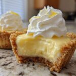 A close-up of a No-Bake Lemon Cream Pie Cup with a bite taken out, showing creamy filling and whipped topping.