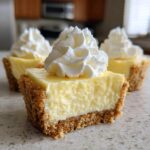 A close-up of a No-Bake Lemon Cream Pie Cup cut in half, showing the creamy filling and graham cracker crust, topped with whipped cream.