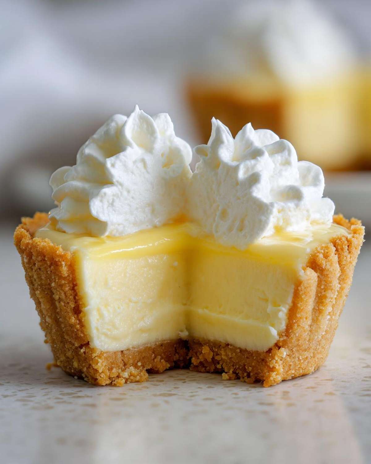 Close-up of a No-Bake Lemon Cream Pie Cup cut in half, showing the creamy filling and graham cracker crust topped with whipped cream.