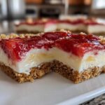A close-up, bitten piece of No-Bake Lemon Strawberry Cheesecake Bark showing graham cracker crust, creamy filling, and strawberry topping.