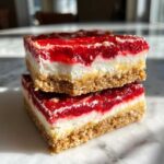 Two stacked squares of No-Bake Lemon Strawberry Cheesecake Bark showing graham cracker crust, cream cheese layer, and bright red topping.