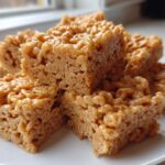A stack of golden brown No-Bake Peanut Butter Rice Cereal Bars served on a white plate.