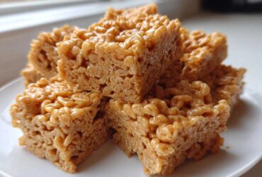 A stack of golden brown No-Bake Peanut Butter Rice Cereal Bars served on a white plate.