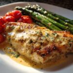 A perfectly cooked fillet of One-Pan Creamy Garlic Butter Tilapia smothered in sauce, served with roasted asparagus and cherry tomatoes.