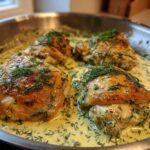 Four golden-brown chicken thighs simmering in a creamy lemon dill sauce, garnished with fresh dill.
