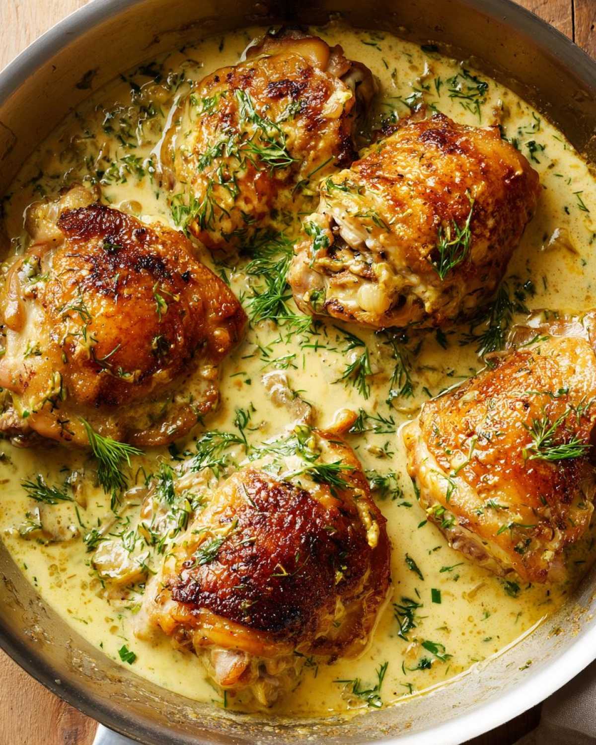 Four crispy-skinned One-Pan Creamy Lemon Dill Chicken Thighs simmering in a rich, yellow sauce topped with fresh dill.