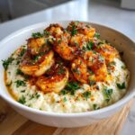 A white bowl filled with creamy grits topped generously with seasoned Cajun shrimp and fresh parsley.
