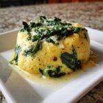 A molded serving of One-Pot Creamy Spinach Parmesan Polenta topped with wilted spinach and grated cheese.