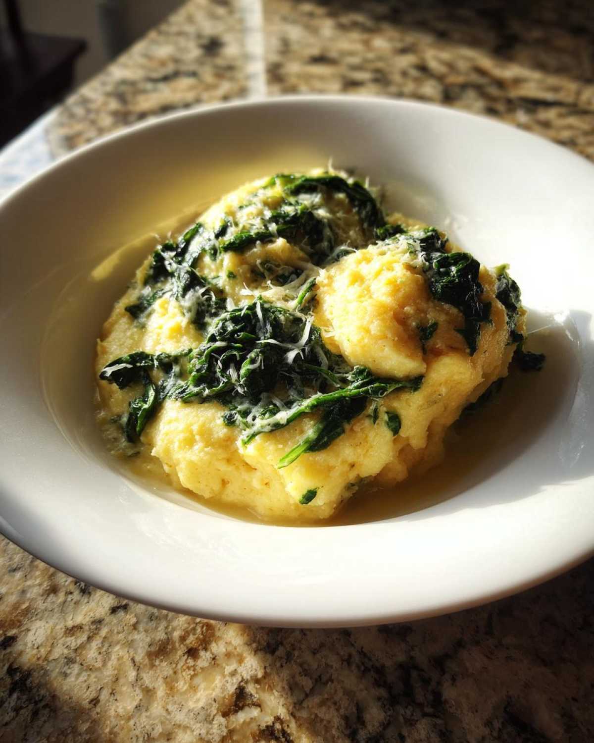 A serving of One-Pot Creamy Spinach Parmesan Polenta topped with wilted spinach and grated cheese in a white bowl.
