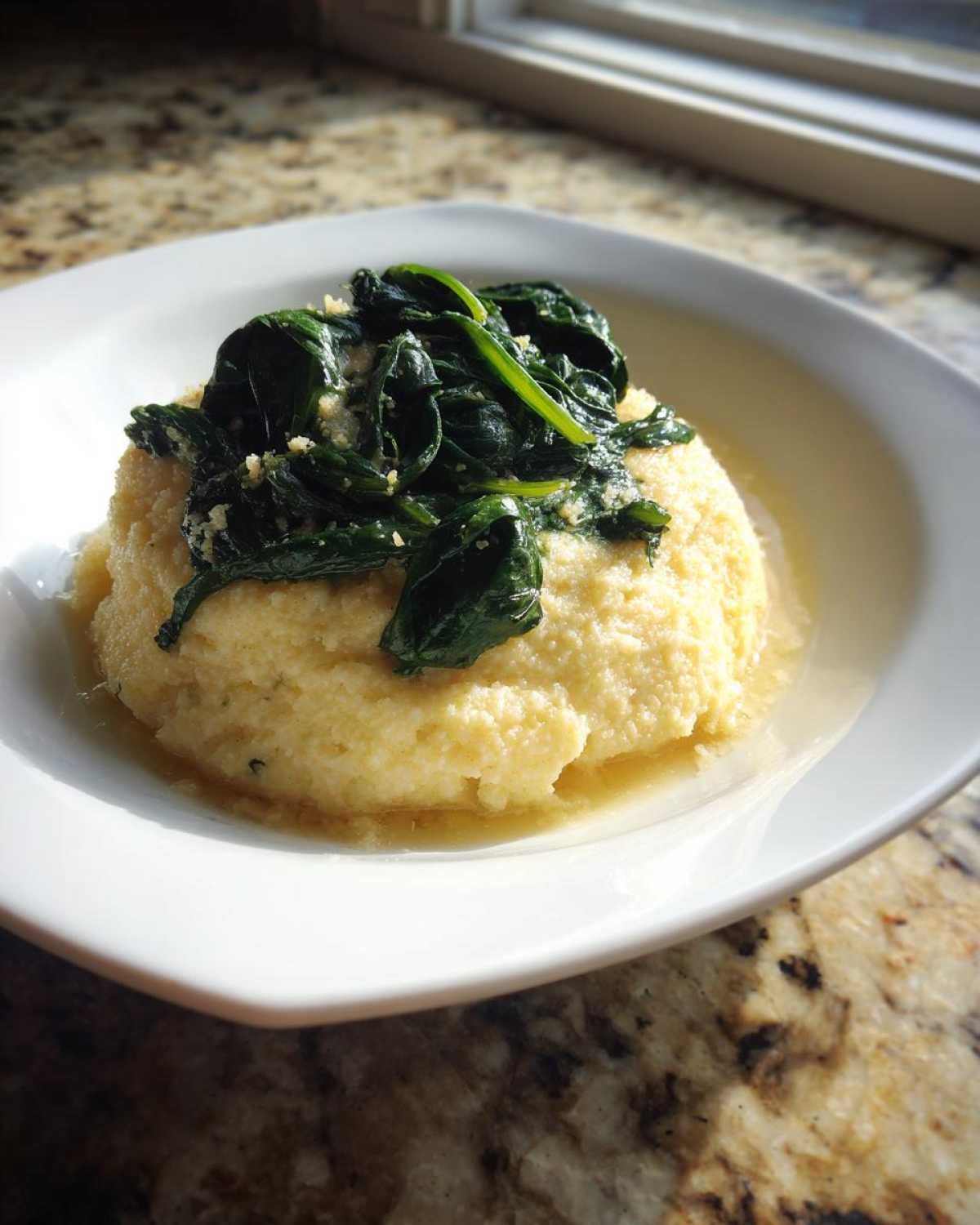 A mound of One-Pot Creamy Spinach Parmesan Polenta topped with wilted spinach and grated cheese in a white bowl.