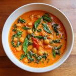 A close-up overhead view of a white bowl filled with One-Pot Creamy Tomato Basil Chickpea Stew, garnished with fresh basil leaves.