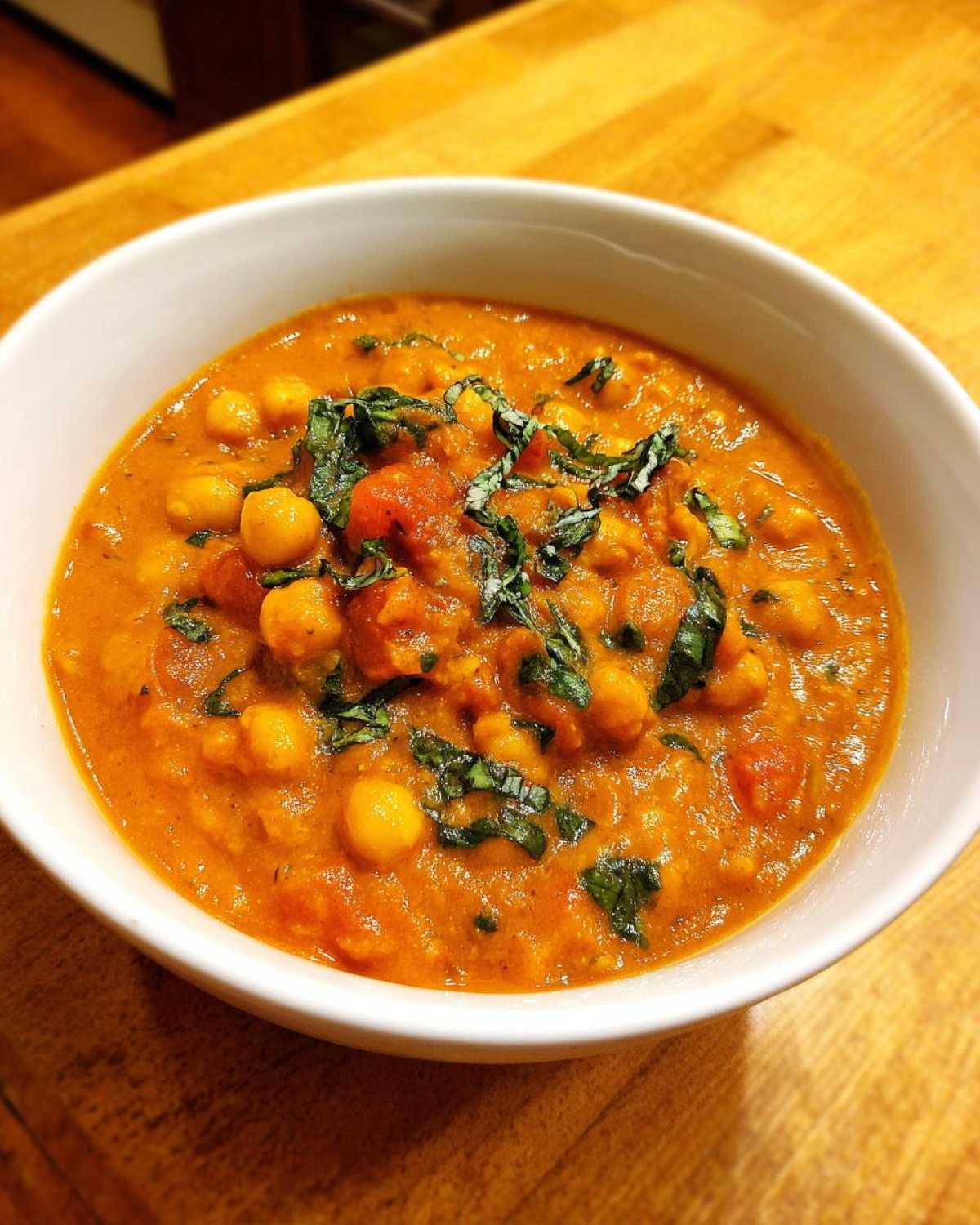 Close-up of a white bowl filled with One-Pot Creamy Tomato Basil Chickpea Stew, garnished with fresh basil.