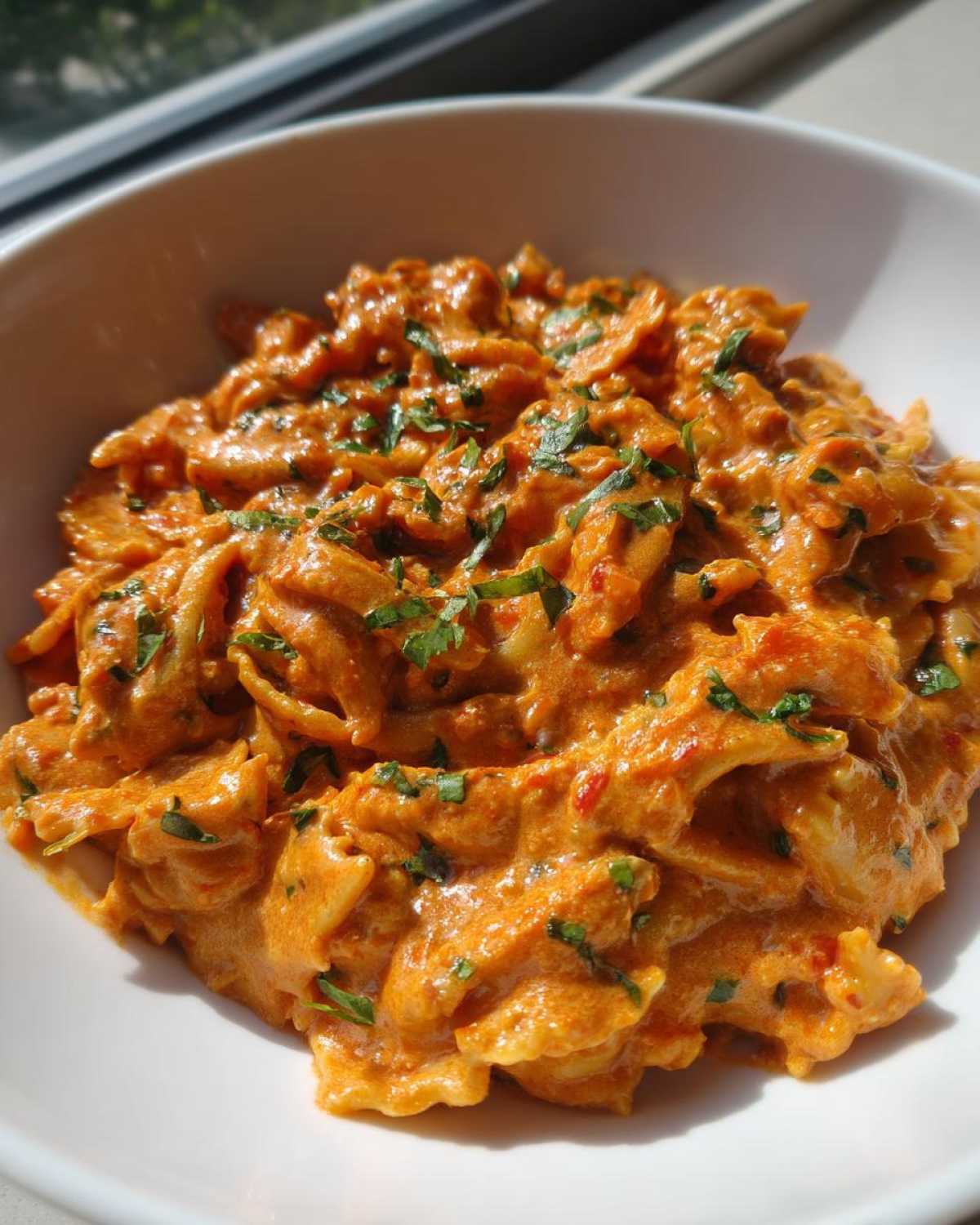 Close-up of One-Pot Creamy Tomato Basil Tortilla Pasta served in a white bowl, garnished with fresh herbs.