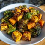 Close-up of Sheet Pan Crispy Honey Mustard Tofu mixed with charred broccoli florets and sweet potato chunks in a white bowl.