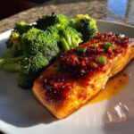 Close-up of a perfectly cooked Sheet Pan Honey Harissa Salmon fillet topped with spicy glaze and green onions, served with roasted broccoli.