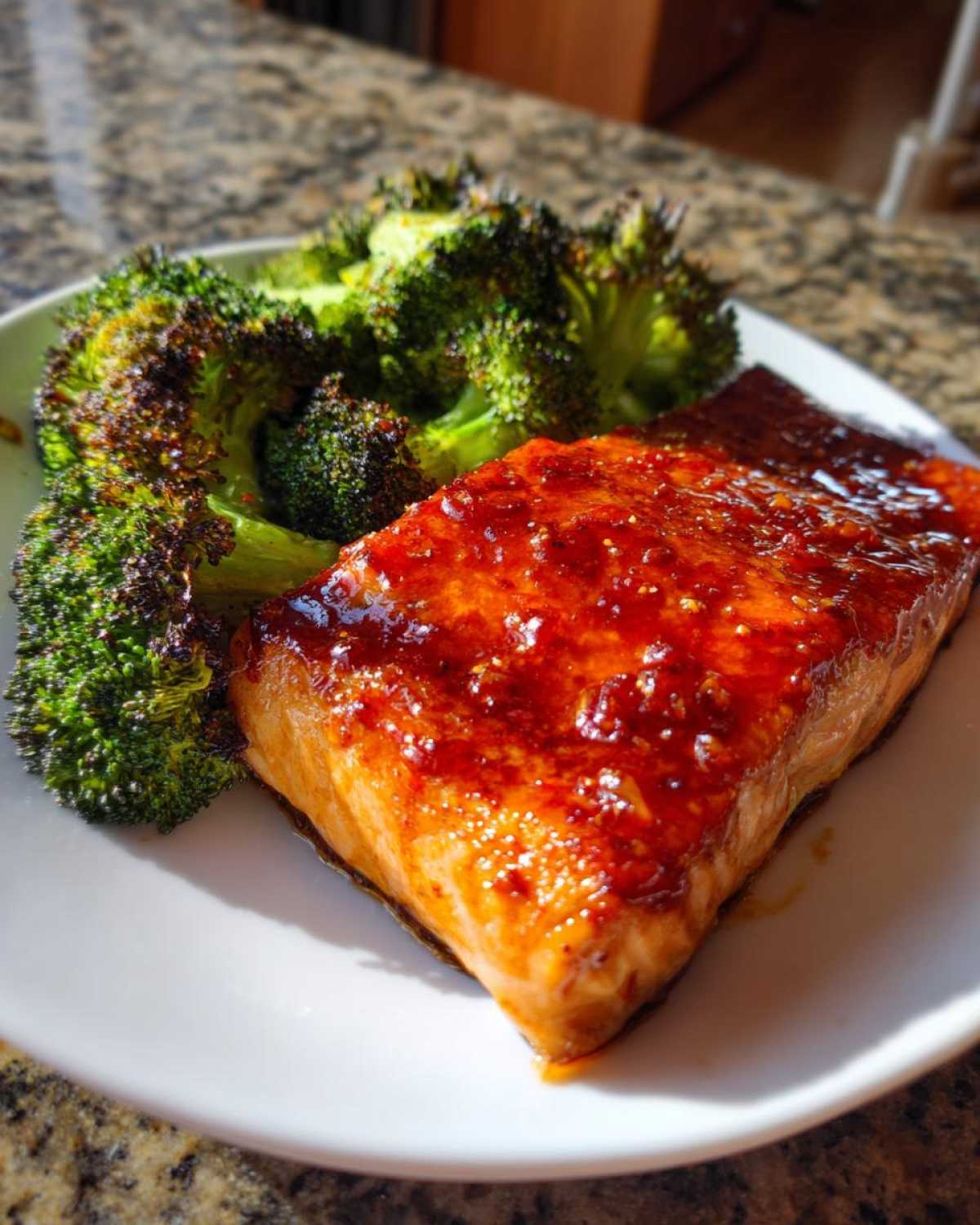 A close-up of a perfectly cooked fillet of Sheet Pan Honey Harissa Salmon next to roasted broccoli florets on a white plate.