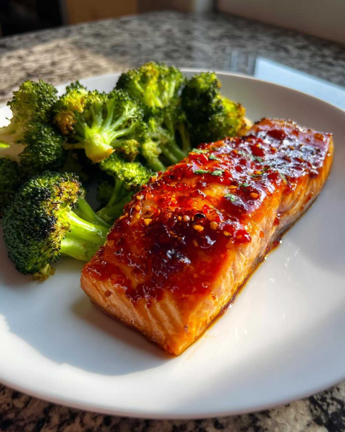 A perfectly cooked fillet of Sheet Pan Honey Harissa Salmon topped with a glossy, spicy glaze, served next to bright green roasted broccoli.
