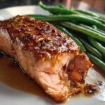 Close-up of a flaky salmon fillet topped with a thick honey mustard glaze next to bright green beans.