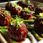Close-up of glazed Sheet Pan Sticky Sesame Meatballs with snap peas, garnished with sesame seeds and green onions.