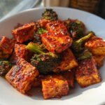 Close-up of crispy Sheet Pan Sweet Chili Tofu with Broccoli florets in a white bowl, sprinkled with sesame seeds.