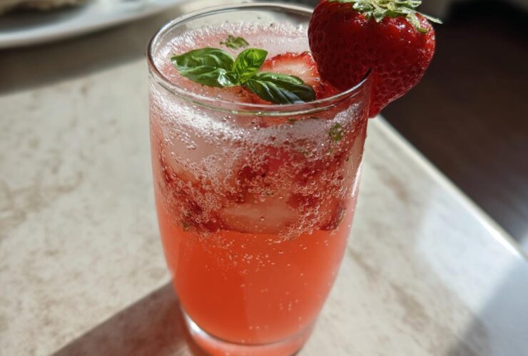 A tall glass filled with vibrant pink Sparkling Strawberry Basil Lemonade, garnished with fresh basil leaves and a whole strawberry.