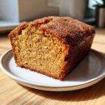 A close-up of a slice of Spiced Apple Cider Donut Loaf, featuring a moist crumb and a sparkling cinnamon sugar crust.