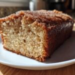A close-up of a moist slice of Spiced Apple Cider Donut Loaf, featuring a golden crumb and a sparkling cinnamon-sugar crust.