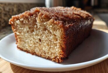 A close-up of a moist slice of Spiced Apple Cider Donut Loaf, featuring a golden crumb and a sparkling cinnamon-sugar crust.