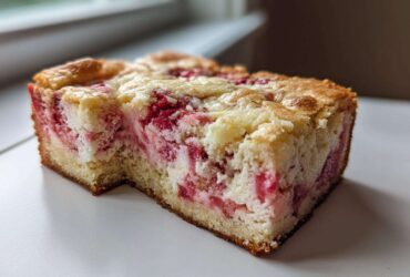 Close-up of a moist slice of Strawberry Earthquake Cake showing the rich pink strawberry swirls mixed with cream cheese batter.