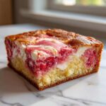 Close-up of a square slice of Strawberry Earthquake Cake with Cream Cheese Swirl showing the moist yellow cake base and pink/white swirled topping.