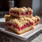Four rich Strawberry Shortcake Streusel Bars stacked on a white plate, showing the crumbly topping and bright red fruit filling.