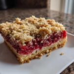 Close-up of a single serving of Strawberry Shortcake Streusel Bars showing a thick layer of bright red fruit filling and a crumbly streusel topping.