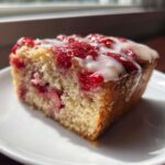 A close-up of a moist slice of Strawberry Yogurt Cake topped with fresh strawberries and white glaze.