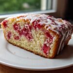 A close-up of a moist slice of Strawberry Yogurt Cake topped with a white vanilla glaze.