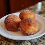 Three golden brown Apple Pie Bombs coated in cinnamon sugar resting on a white plate.