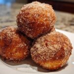 Three golden-brown Apple Pie Bombs heavily coated in cinnamon sugar, stacked on a white plate.