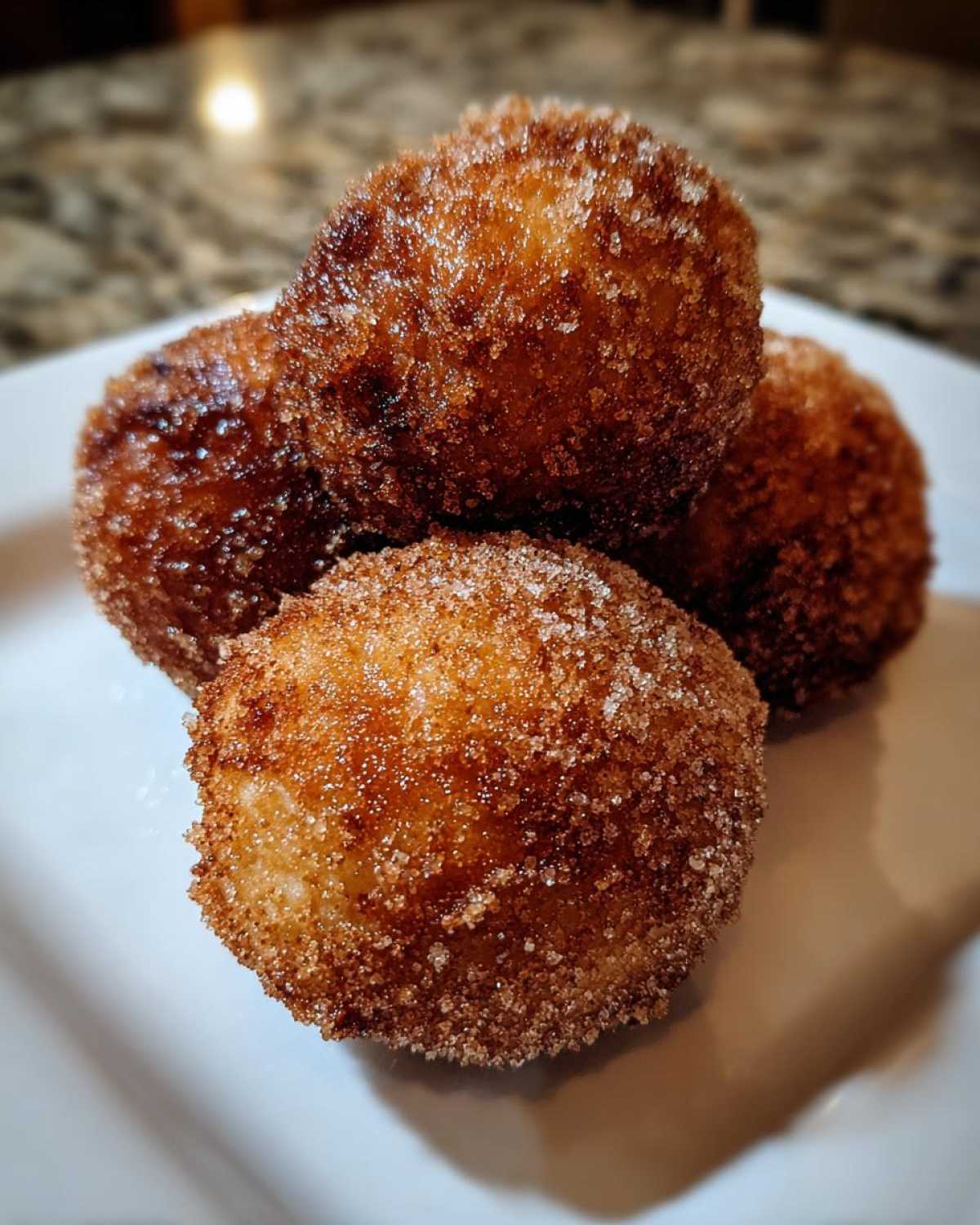 Four golden-brown, deep-fried Apple Pie Bombs heavily coated in cinnamon sugar resting on a white plate.