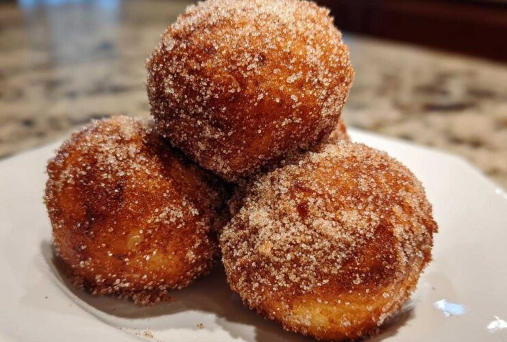 Three golden-brown Apple Pie Bombs heavily coated in cinnamon sugar, stacked on a white plate.