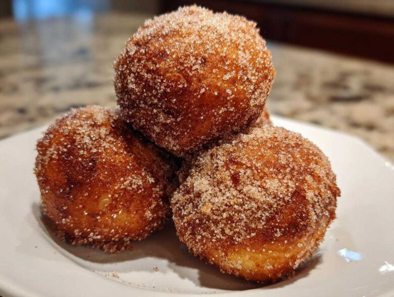 Three golden-brown Apple Pie Bombs heavily coated in cinnamon sugar, stacked on a white plate.