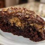 Close-up of a rich slice of Texas Tornado Cake showing dark chocolate cake, gooey filling, and chocolate frosting topped with chopped pecans.