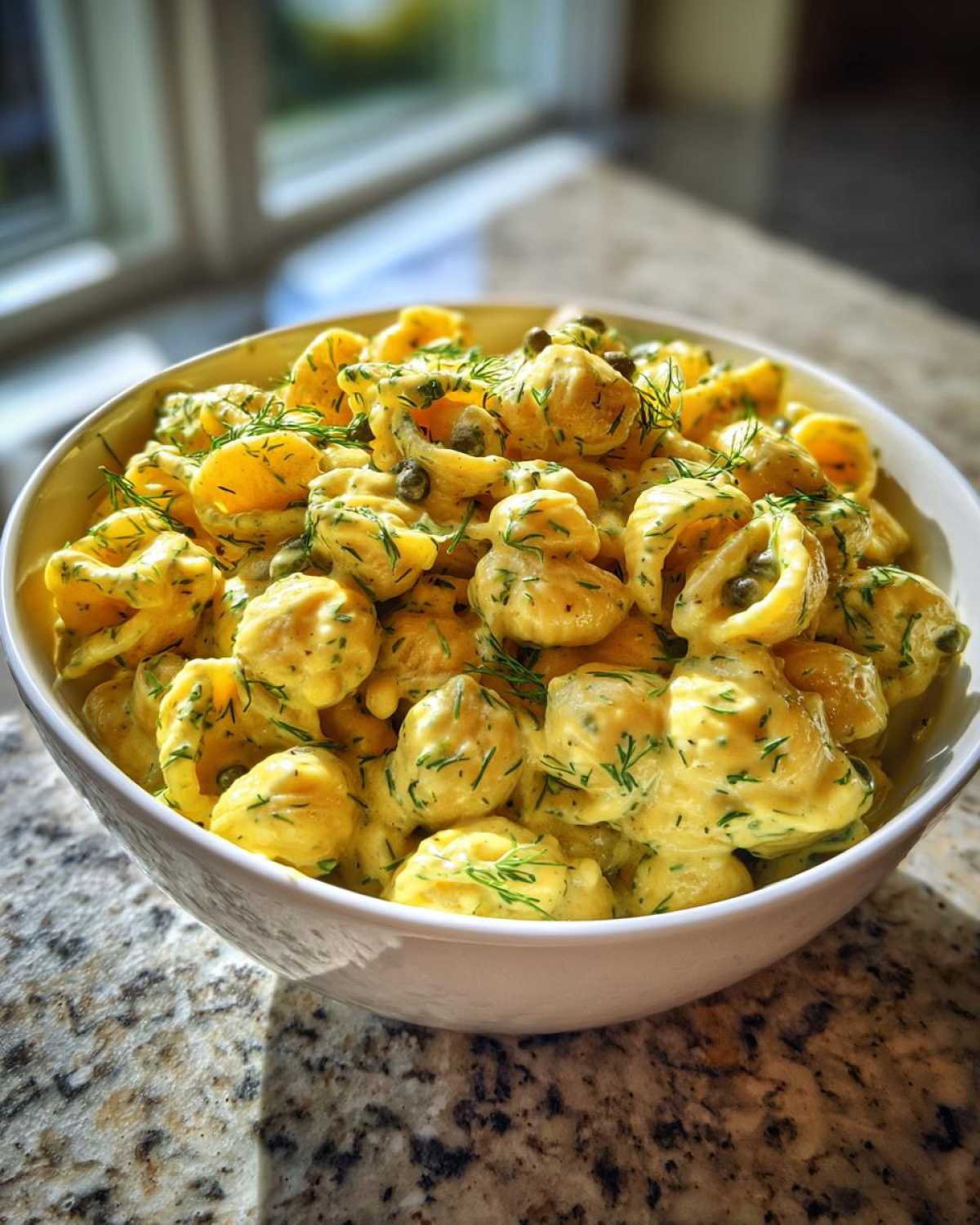 A white bowl filled with Vegan Creamy Lemon Chickpea Pasta Salad, topped with fresh dill and capers.