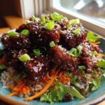 Close-up of a Vegan Crispy Sesame Tempeh Bowl featuring glazed tempeh pieces over brown rice and mixed greens.